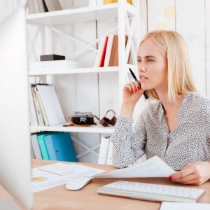 Business woman holding pen and looking at computer screen