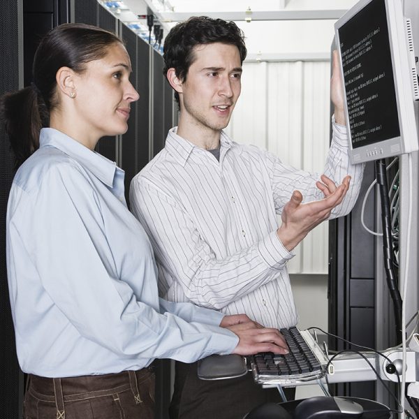 Caucasian man and woman computer techniciians checking data on computer servers in a computer server farm.