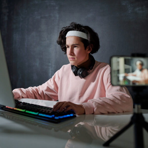 Young serious man in casualwear looking at computer screen while typing by desk